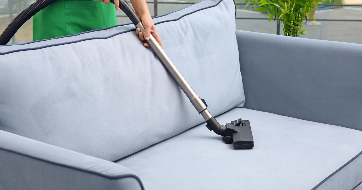 Aspiração profunda de um sofá azul claro com um aspirador de mão com bocal apropriado para estofados, enfatizando a manutenção da higiene e cuidado com móveis.